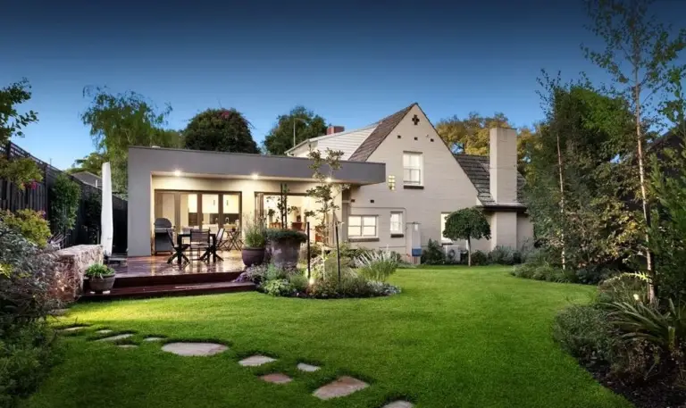 Rear garden and timber deck beside a two-storey weatherboard home at dusk