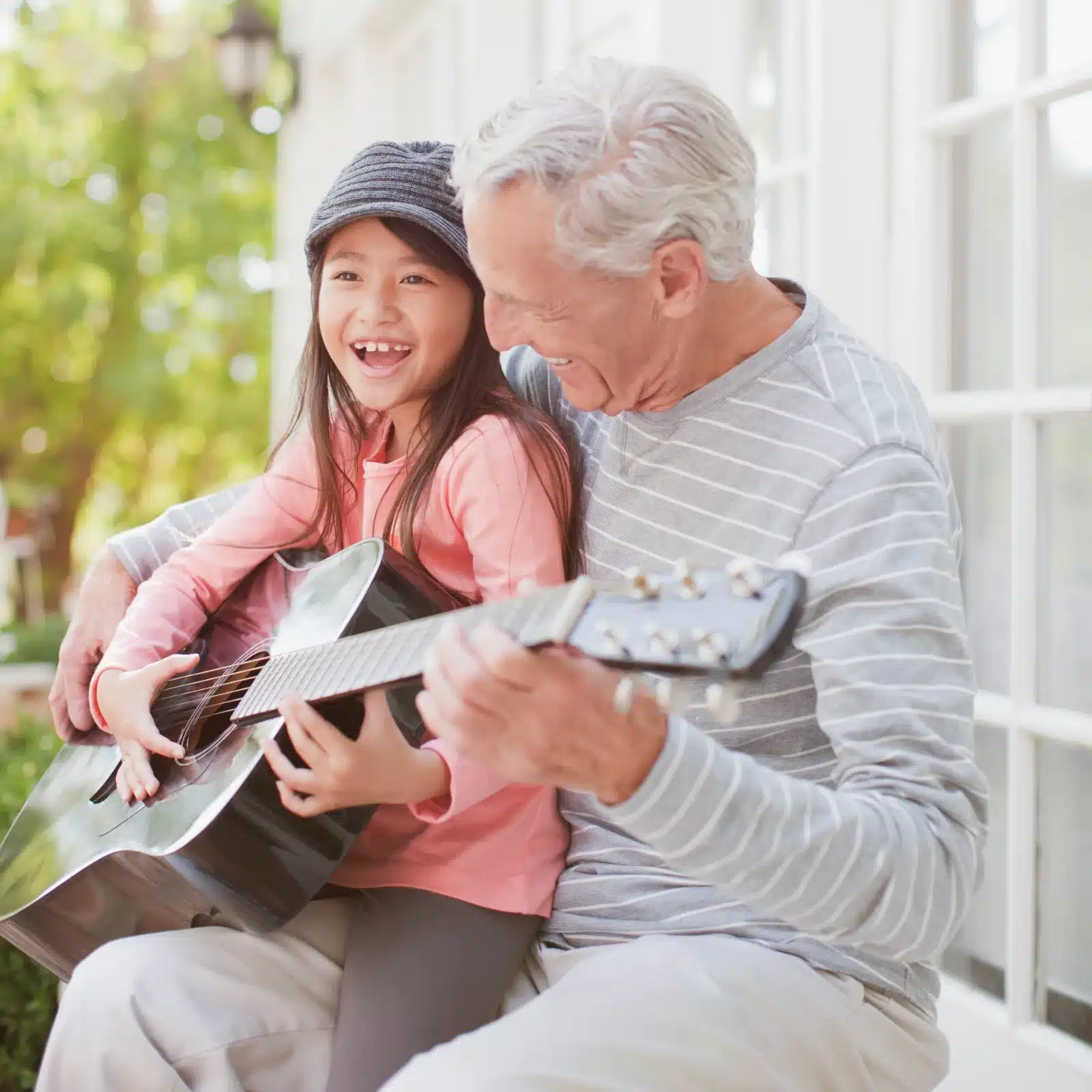 Older man and young girl smiling together while playing an acoustic guitar
