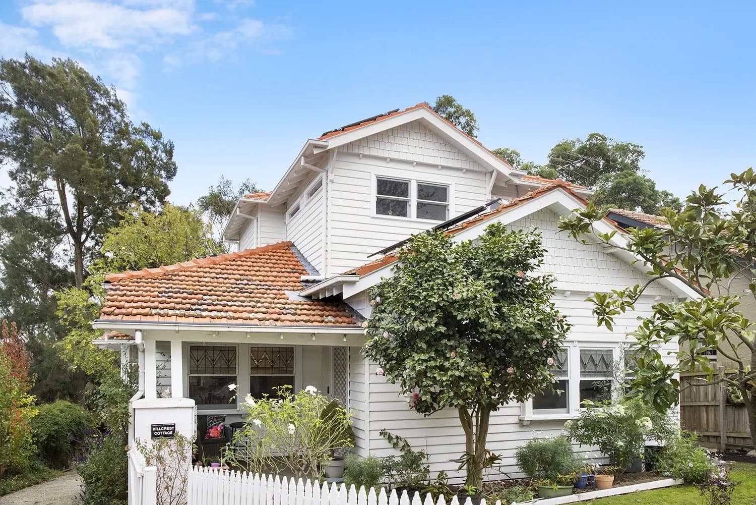 White weatherboard home with a tiled roof, upper-storey gable and picket fence