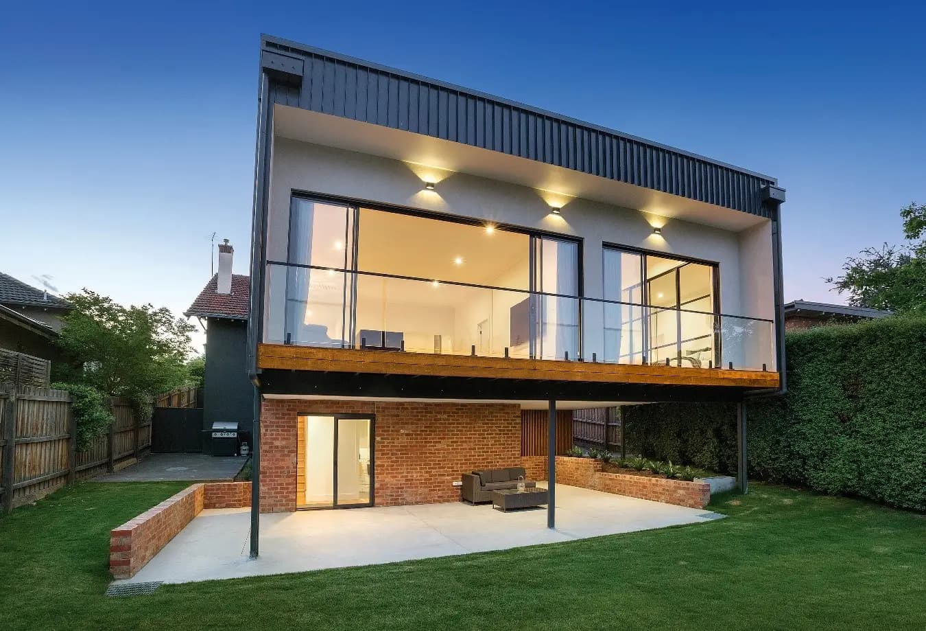Two-storey rear extension with a glass balcony and covered patio overlooking a lawn