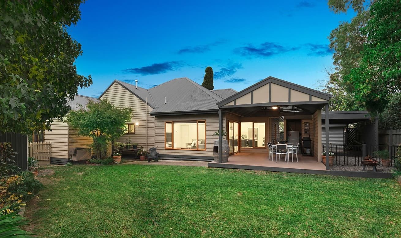 Weatherboard home with a covered outdoor dining area overlooking a lawn at dusk